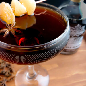 dark cocktail in a coupe glass in front of a bottle of maple syrup