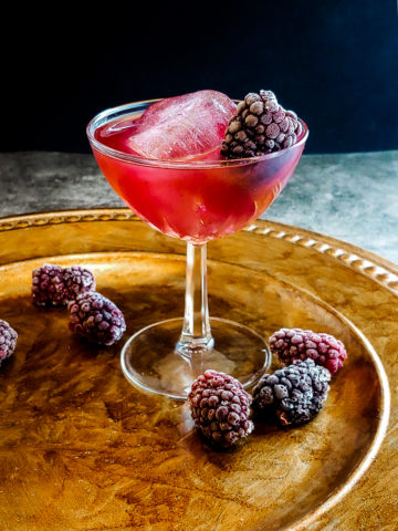 pink cocktail in a glass with ice and blackberry