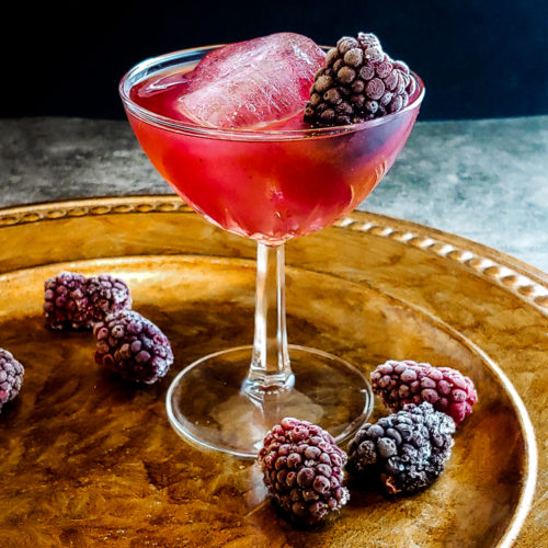 pink cocktail in a glass with ice and blackberry