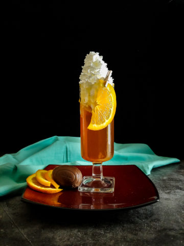 cocktail in a tall glass with whipped cream and orange