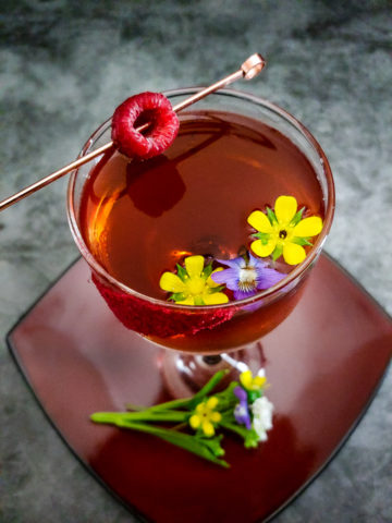 cocktail in coupe garnished with flowers and raspberry