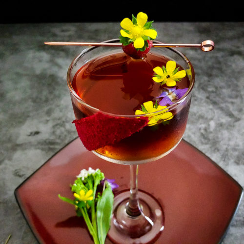 cocktail in coupe garnished with flowers and raspberry