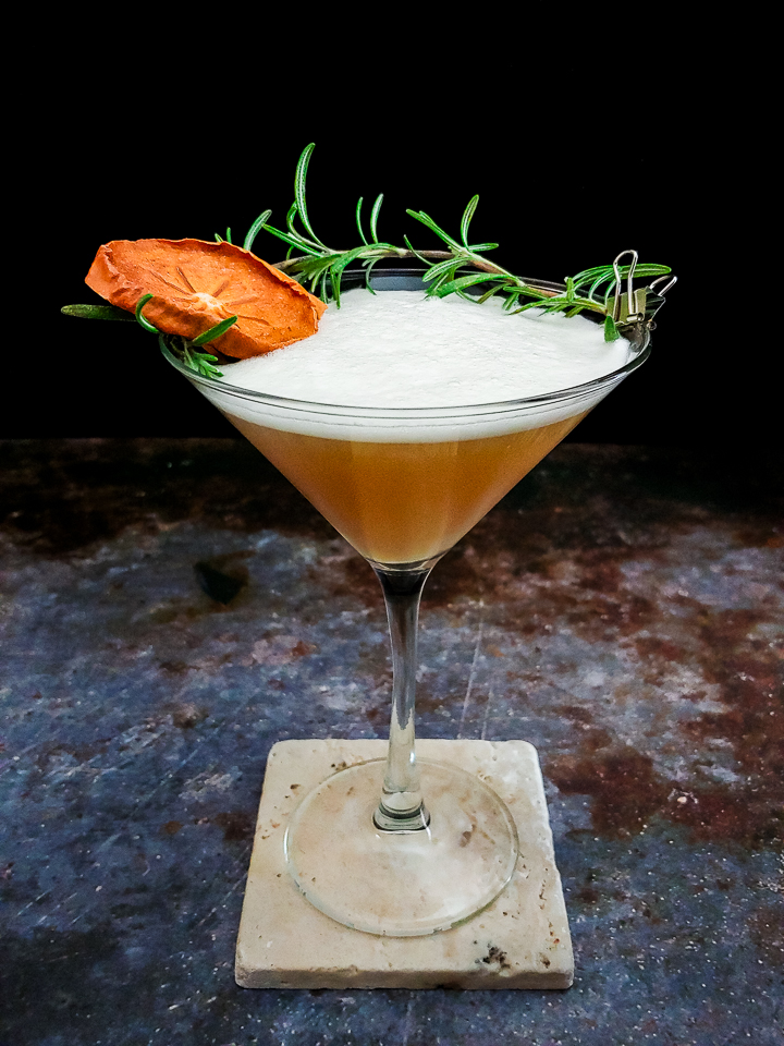 cocktail in martini glass with rosemary and dried persimmon