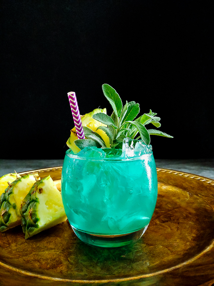 blue cocktail with pineapple sage garnish