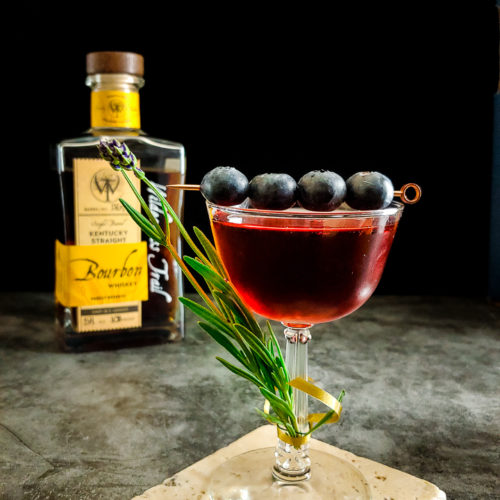 cocktail with lavender and blueberry garnish, Wilderness Trail bourbon in background