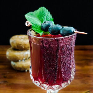 magenta cocktail garnished with blueberries and mint