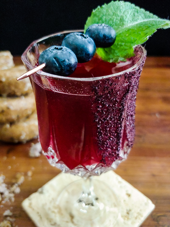 magenta cocktail garnished with blueberries and mint