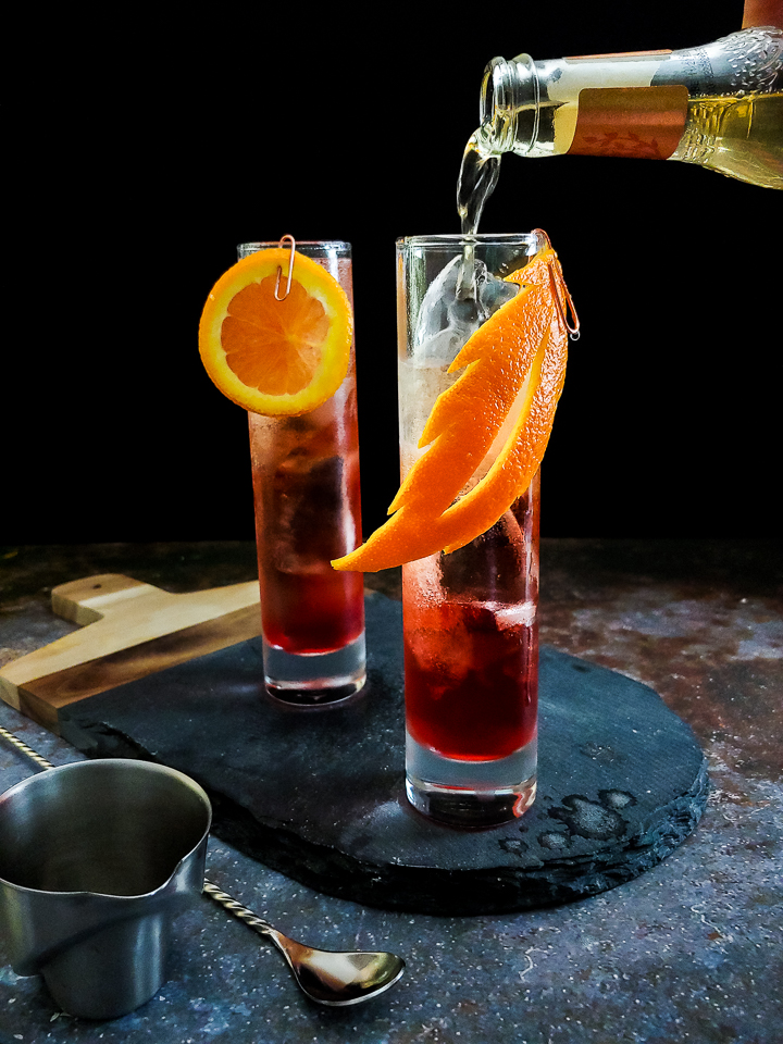 magenta whiskey cocktail in highball glass with orange garnish