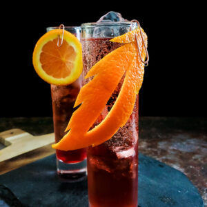 magenta whiskey cocktail in highball glass with orange garnish