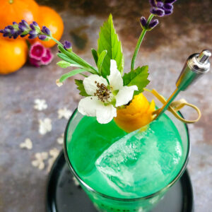 aqua green cocktail in highball glass with orange and lavender garnish