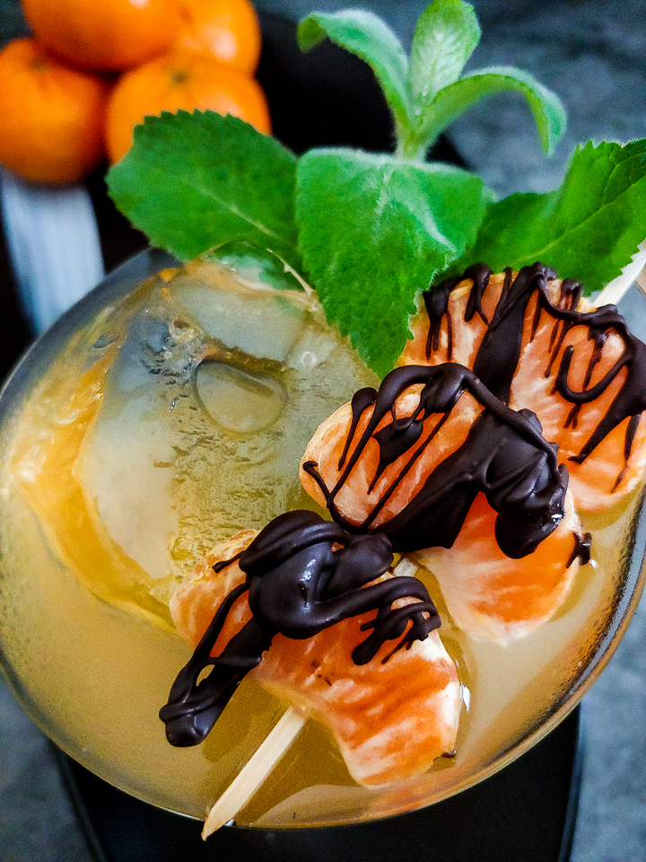 orange-yellow cocktail with ice and chocolate covered mandarins and mint garnish