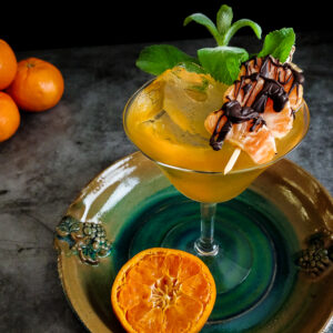 orange-yellow cocktail with ice and chocolate covered mandarins and mint garnish
