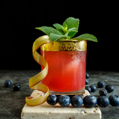 pink cocktail with rhubarb curl, mint and blueberry garnish