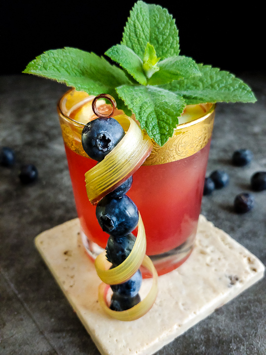 pink cocktail with rhubarb curl, mint and blueberry garnish