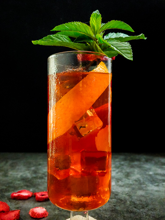 whiskey cocktail with strawberry, orange and mint garnish