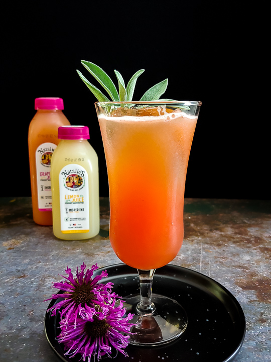 orange-hued whiskey sour with sage leaves and bee balm flowers