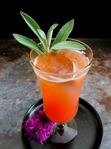 orange-hued whiskey sour with sage leaves and bee balm flowers