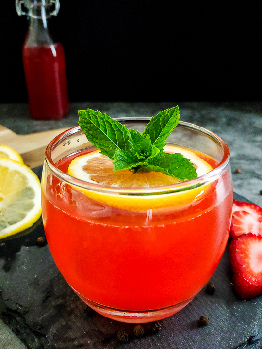 red cocktail with strawberry, mint and lemon garnish