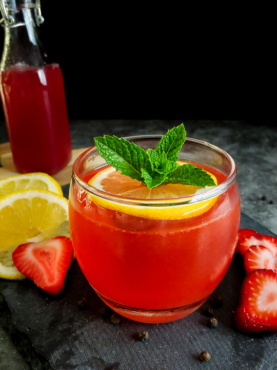 red cocktail with strawberry, mint and lemon garnish