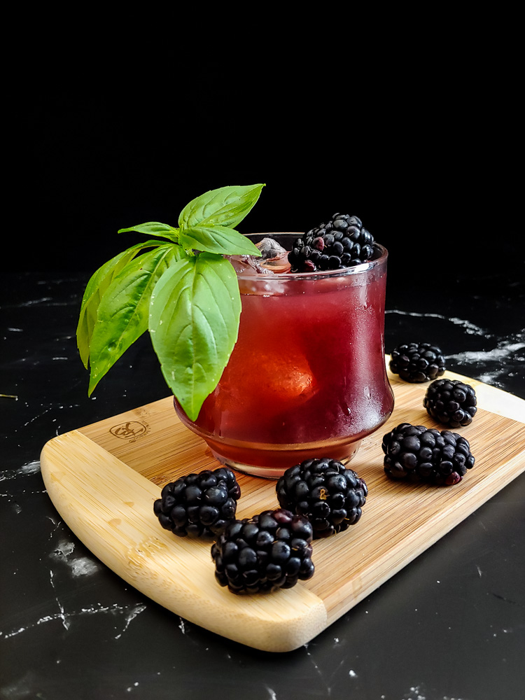 blackberry old fashioned cocktail in a rocks glass with ice and basil and blackberries