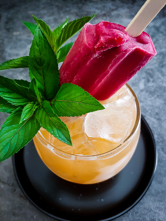 peach cocktail with a raspberry popsicle garnish