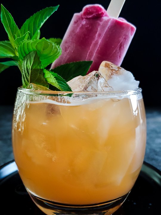 peach cocktail with a raspberry popsicle garnish