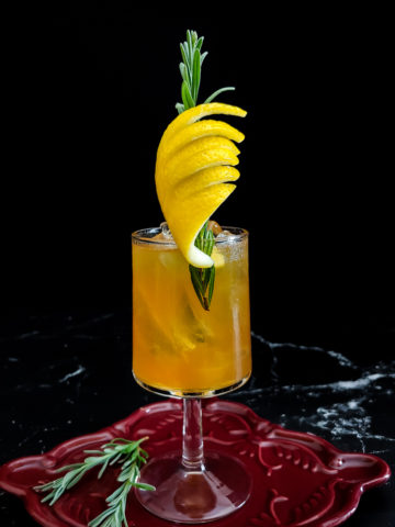 Old fashioned in a wine glass with ice, lemon peel and lavender sprig