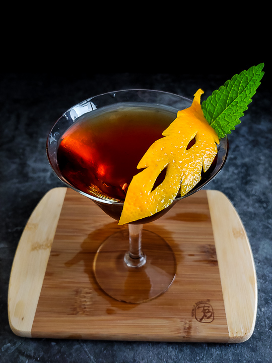 manhattan cocktail with orange leaf cutout garnish