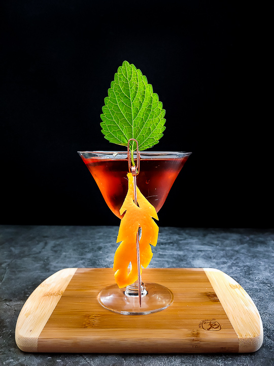 manhattan cocktail with orange leaf cutout garnish