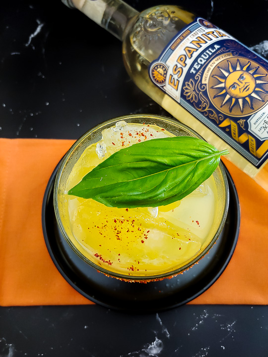 mango cocktail with spiced swath and basil leaf, and tequila bottle