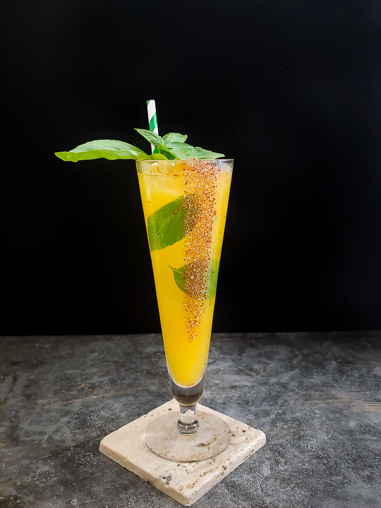 yellow mango cocktail with basil leaves and red chili rim
