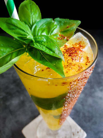 yellow mango cocktail with basil leaves and red chili rim