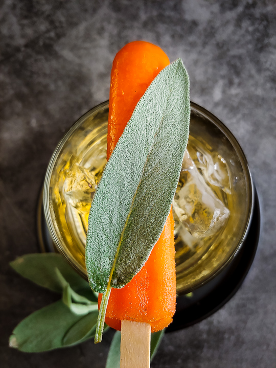 mezcal cocktail with orange popsicle and sage leaf on top