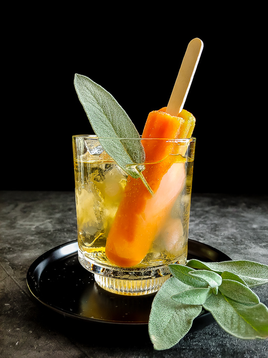mezcal cocktail with orange popsicle and sage leaf on top
