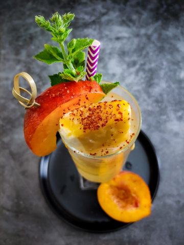peach cocktail in tall glass garnished with peach, mango popsicle and mint
