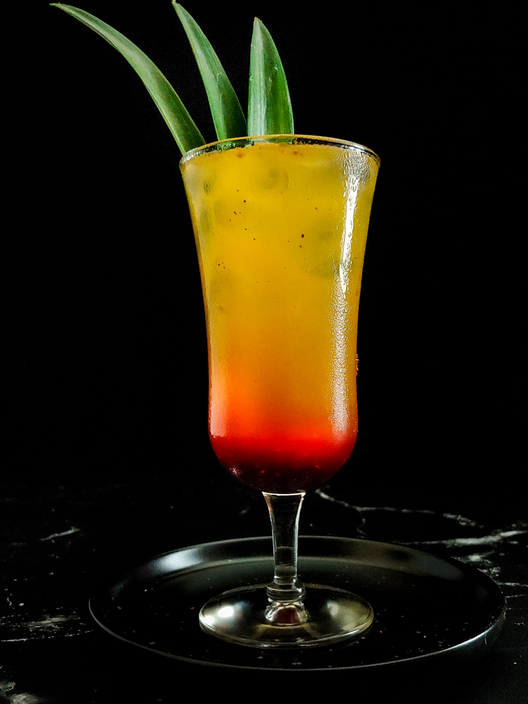 smoky tequila sunrise photo with cocktail gradient from yellow to red, with red powder and green frond garnish