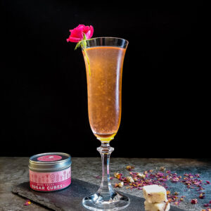light pink cocktail in champagne flute with rose garnish and sugar cubes