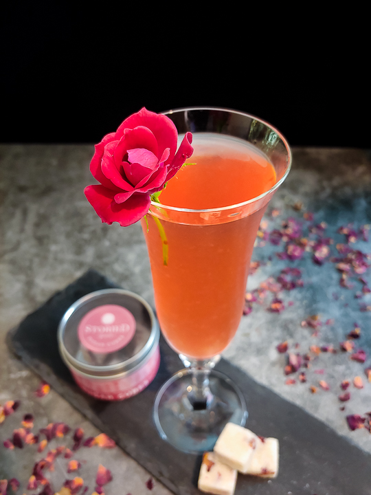 light pink cocktail in champagne flute with rose garnish and sugar cubes
