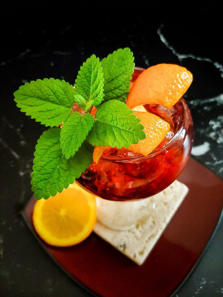 Bitter Bourbon Spritz red cocktail in a wine glass with orange and mint garnish