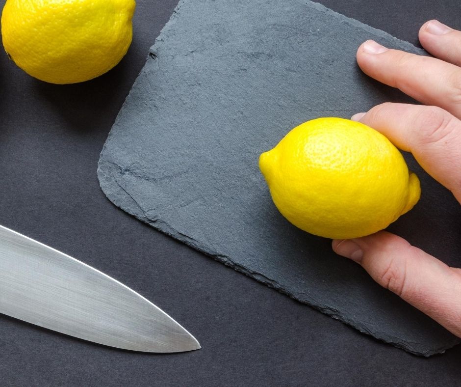 Hand holding a lemon on a cutting surface with knife