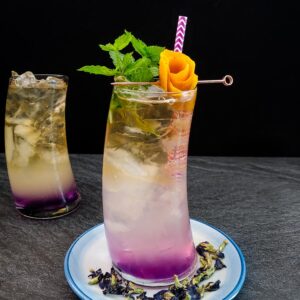 Bourbon cooler in tall glass with purple, white and yellow layer, orange rose and mint garnish