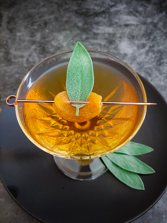 Uncle Nearest Apricot Manhattan cocktail in a coupe glass with apricot with a sage leaf