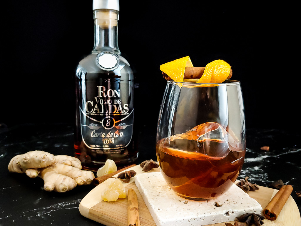 rum old fashioned on a cutting board with spices and bottle of rum
