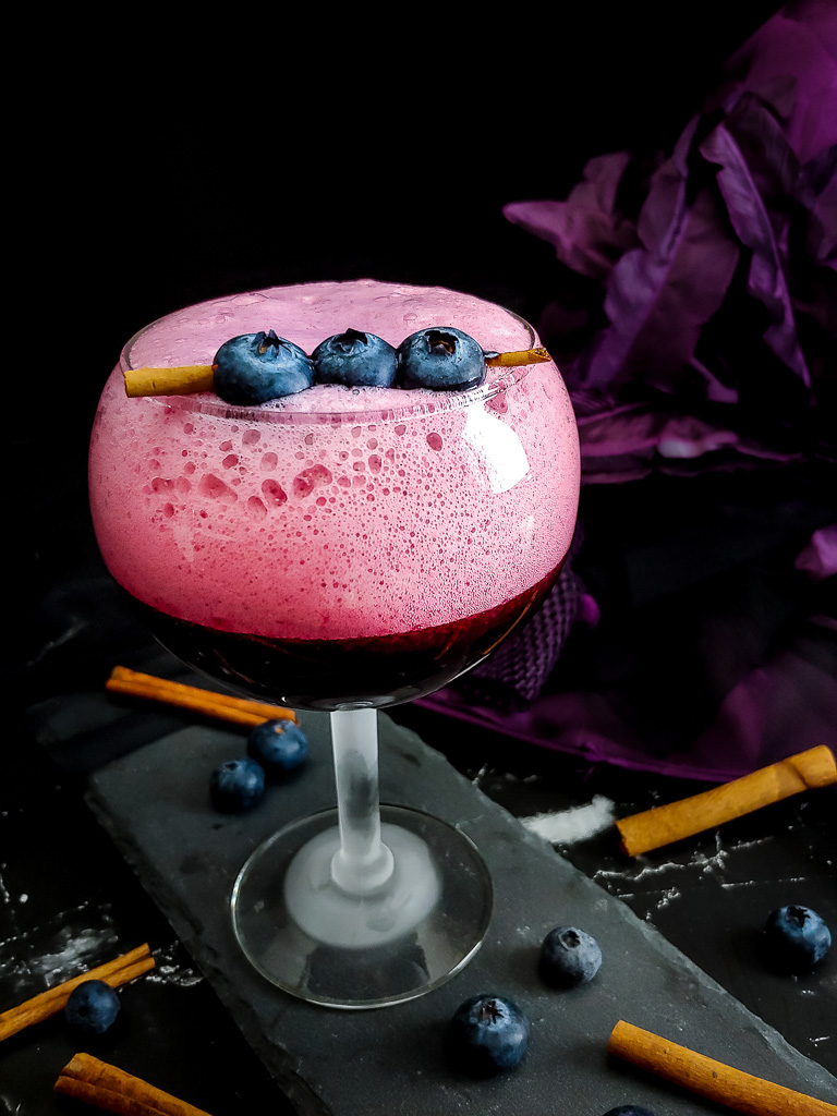 Blueberry Sour with cinnamon stick and blueberry garnish in tall, round goblet