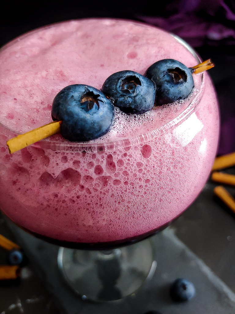 Blueberry Sour with cinnamon stick and blueberry garnish in tall, round goblet