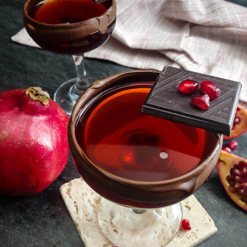 Chocolate Pomegranate Manhattan in a coupe with chocolate rim and pomegranate garnish