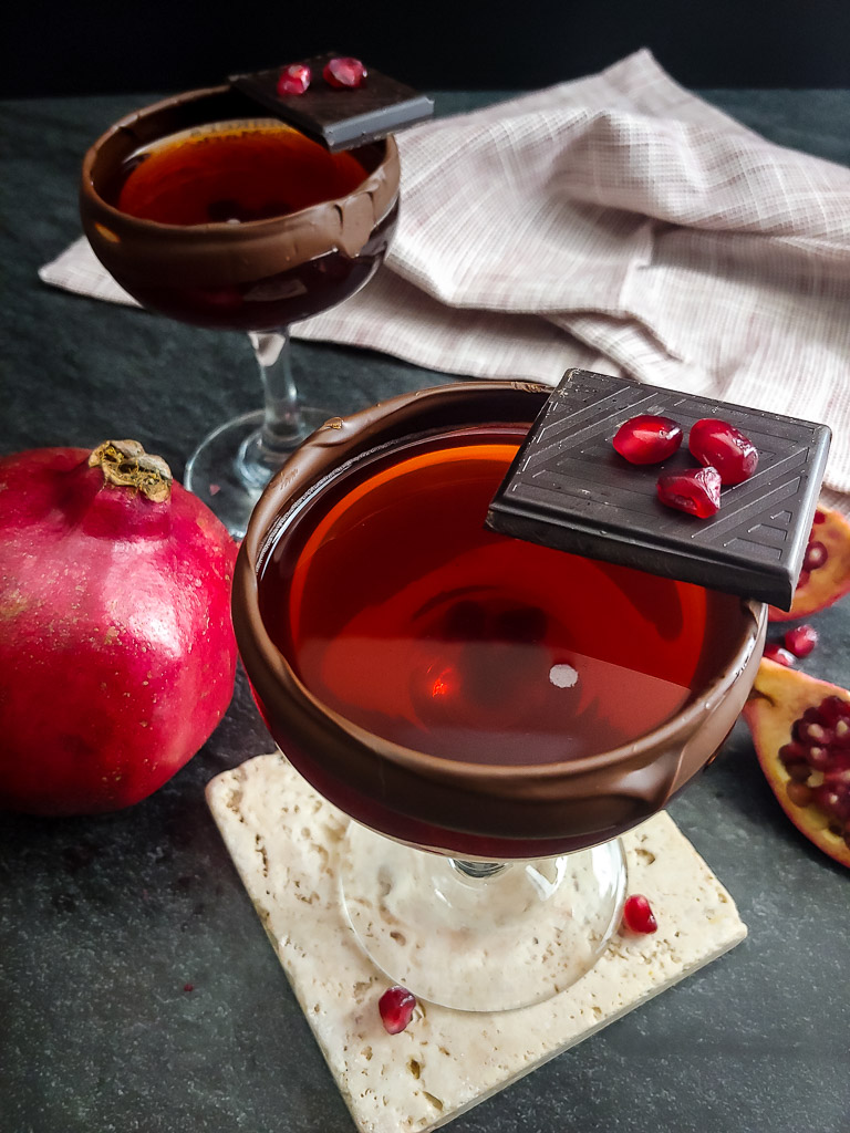 Chocolate Pomegranate Manhattan in a coupe with chocolate rim and pomegranate garnish