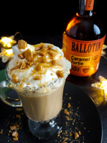 Boozy Caramel Brulee Latte topped with whipped cream, caramel drizzle and toffee with Ballotin Caramel Turtle whiskey bottle