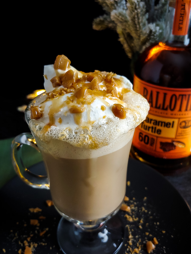 Boozy Caramel Brulee Latte topped with whipped cream, caramel drizzle and toffee with Ballotin Caramel Turtle whiskey bottle