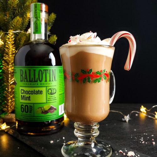 Boozy Peppermint Mocha Latte topped with whipped cream and candy cane pieces with bottle of Ballotin Chocolate Mint Whiskey